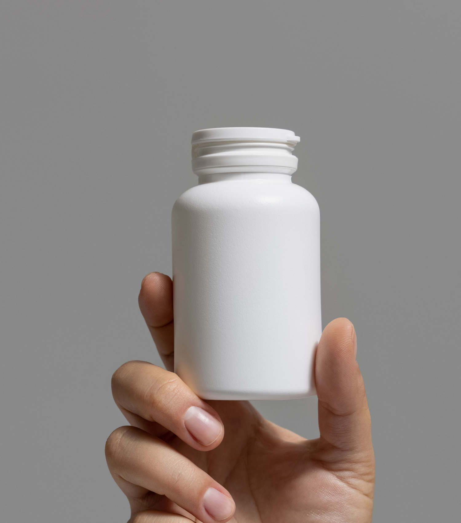Female hand holding a plain white plastic pill bottle against a gray background